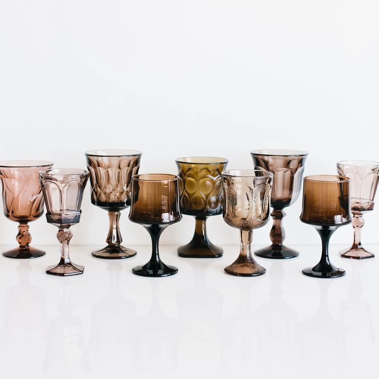 an assortment of wine goblets are lined up in a row on a white surface