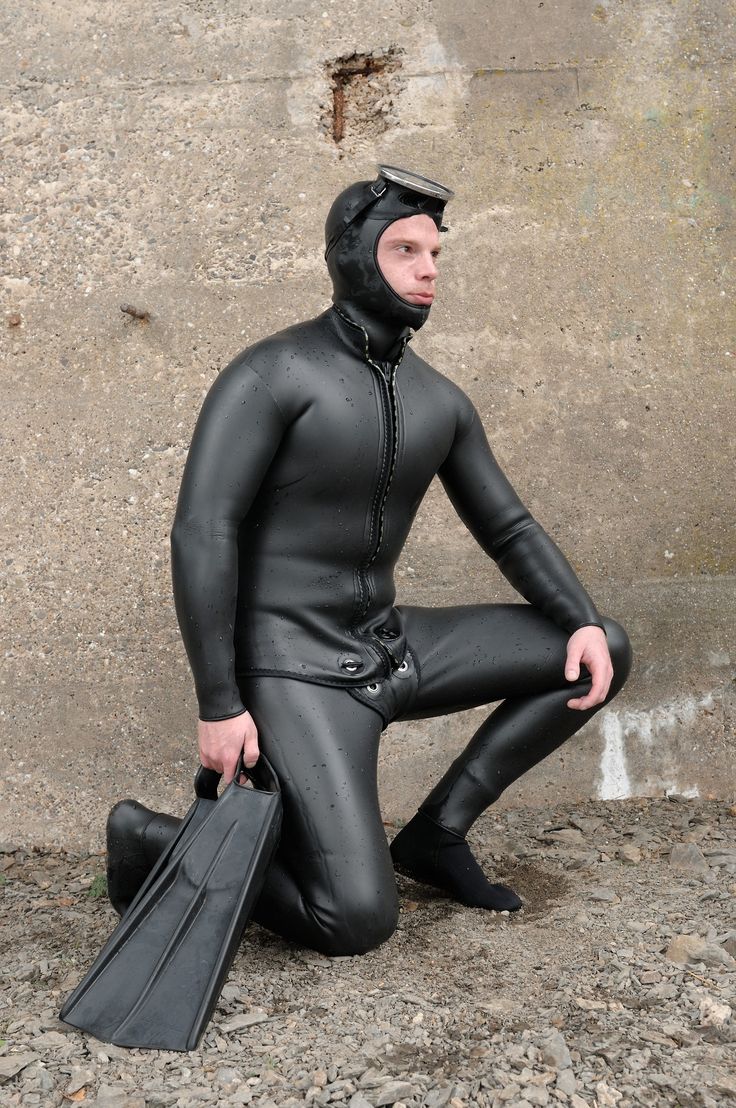 a man in a wet suit holding a briefcase and wearing a black helmet is sitting on the ground