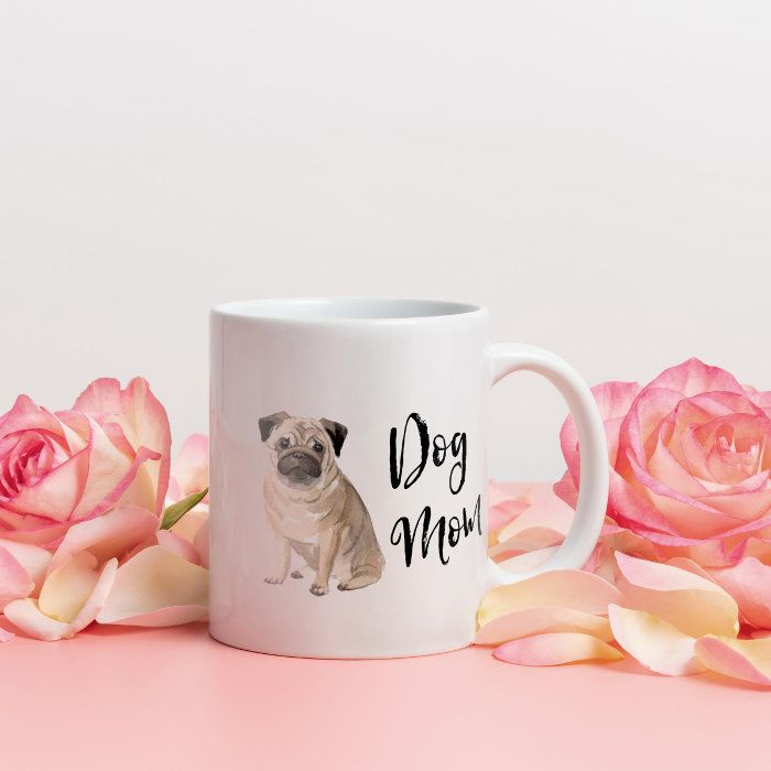 a white coffee mug with a pug mom design on it next to pink roses