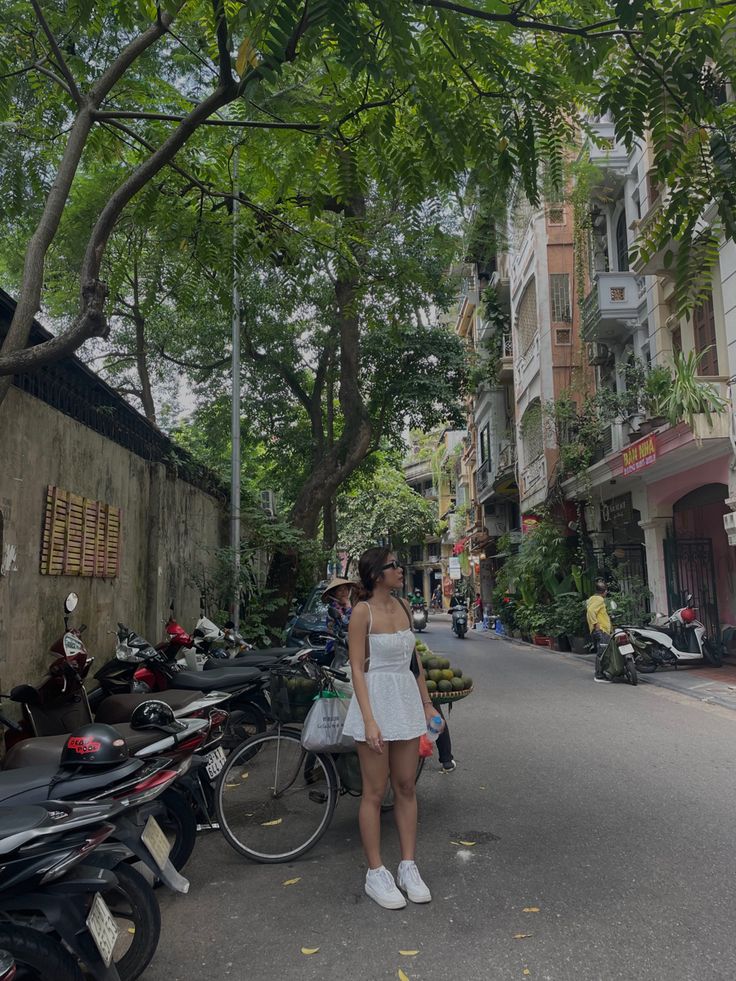 a woman standing in the middle of a street next to parked motor scooters