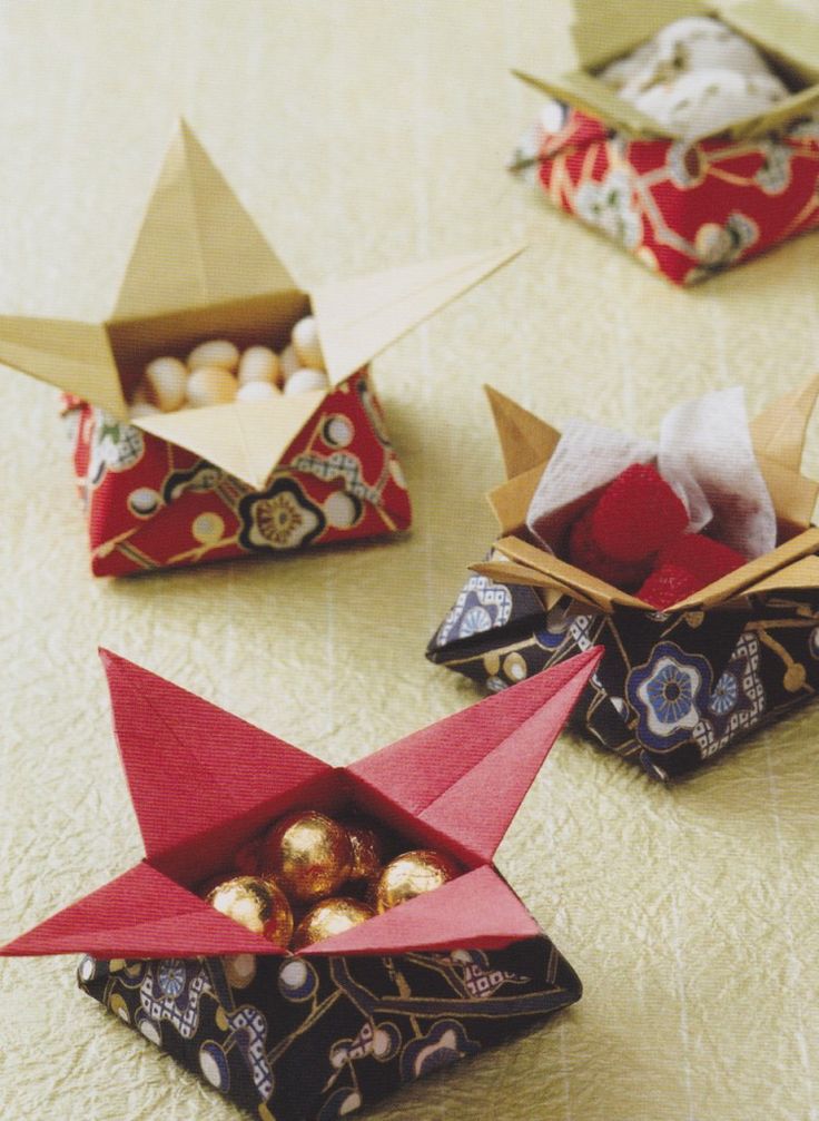 three origami boats are sitting on the table with their lids open and one is filled with chocolates