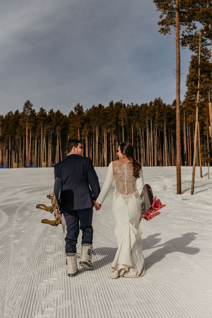 a bride and groom walking through the snow with their skis in tow holding hands