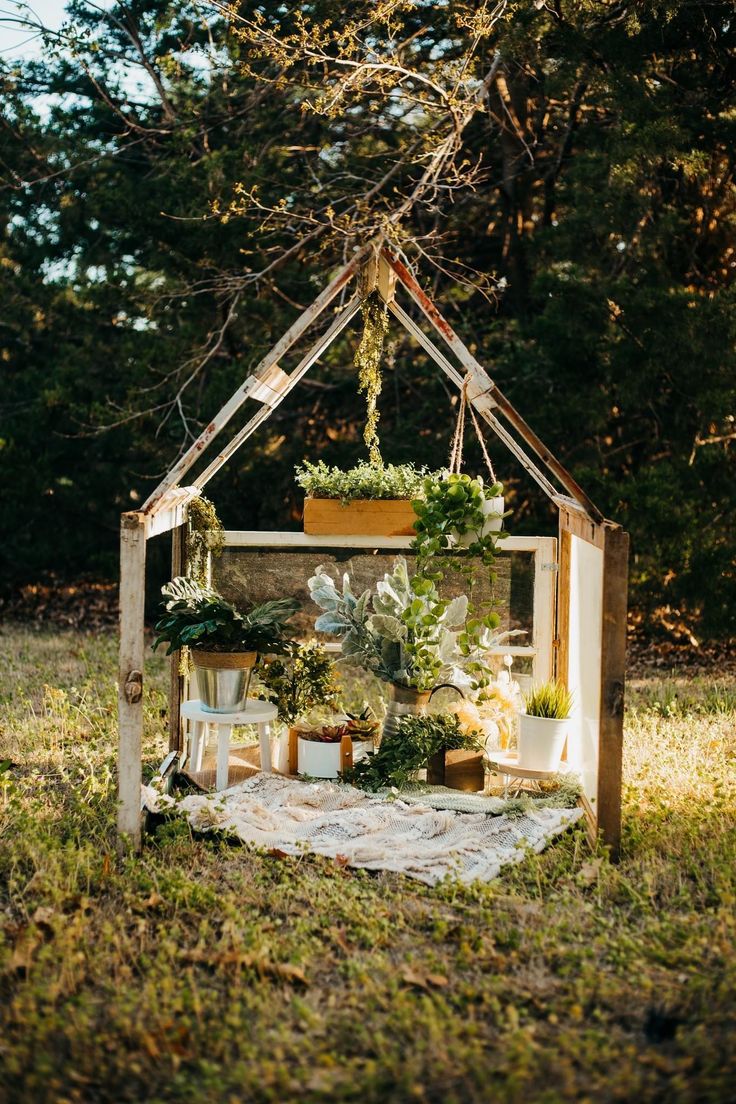 a small wooden structure with plants in it on top of the grass and trees behind it