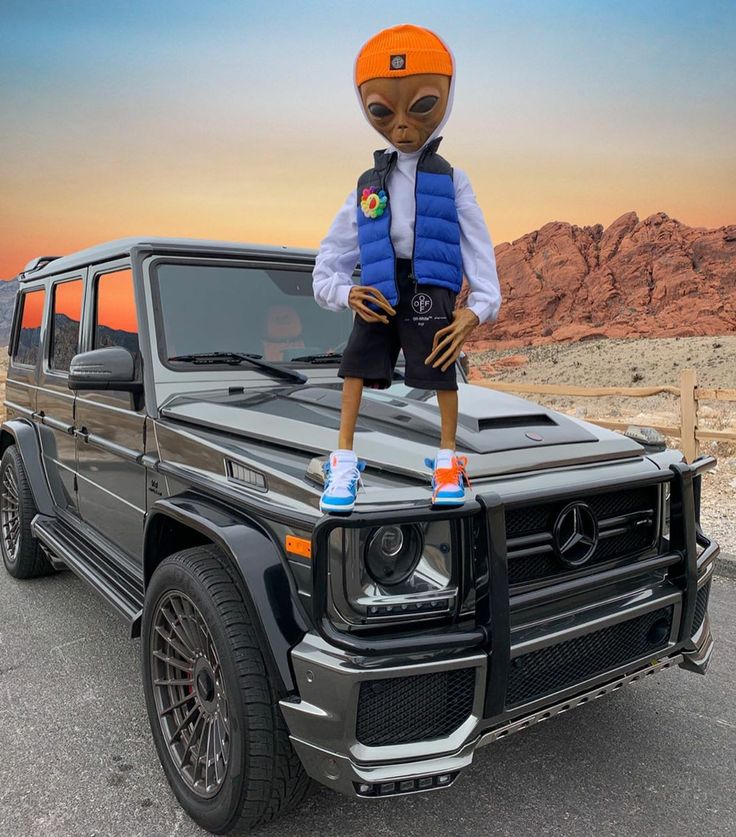 an alien standing on the hood of a mercedes g - class in front of a desert landscape