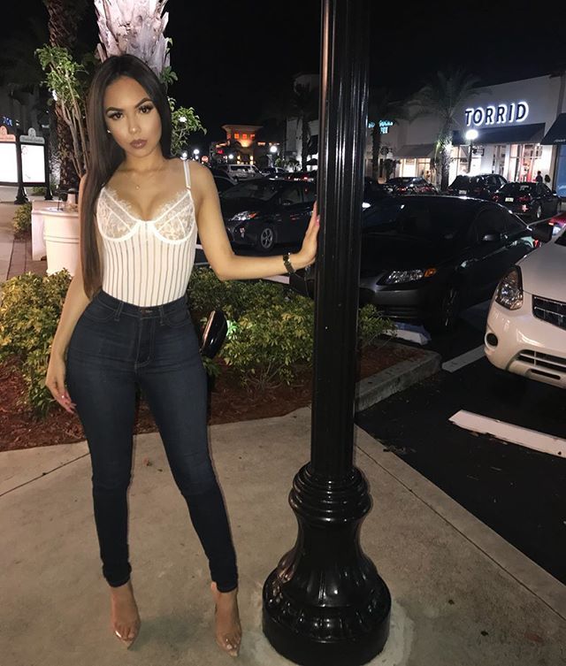 a woman standing next to a street light in front of a car dealership at night