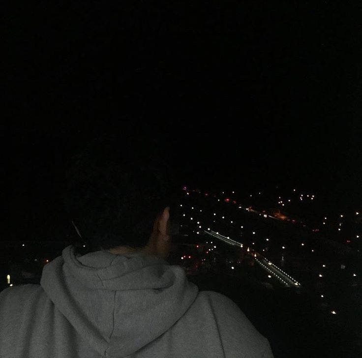 a person wearing a hoodie looking at the city lights from a high vantage point