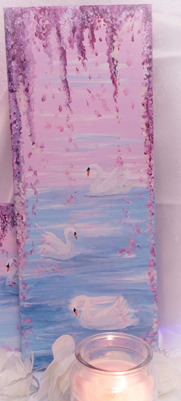 a candle sits next to a painting with swans on it