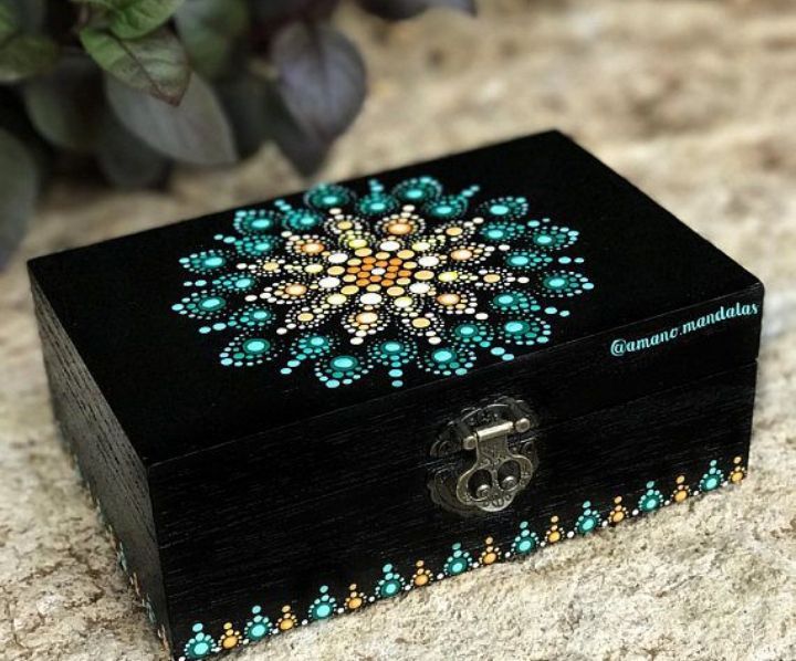 a black box with green jewels on it sitting on a table next to a plant