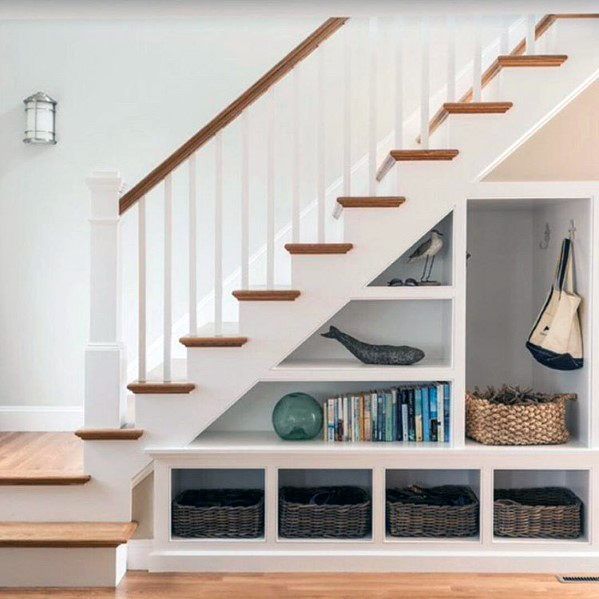 a book shelf under the stairs with baskets and books on it next to a stair case