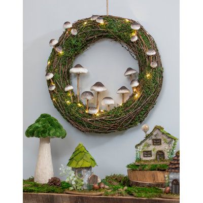 a wreath with mushrooms and fairy lights hanging on the wall next to a shelf filled with miniature houses