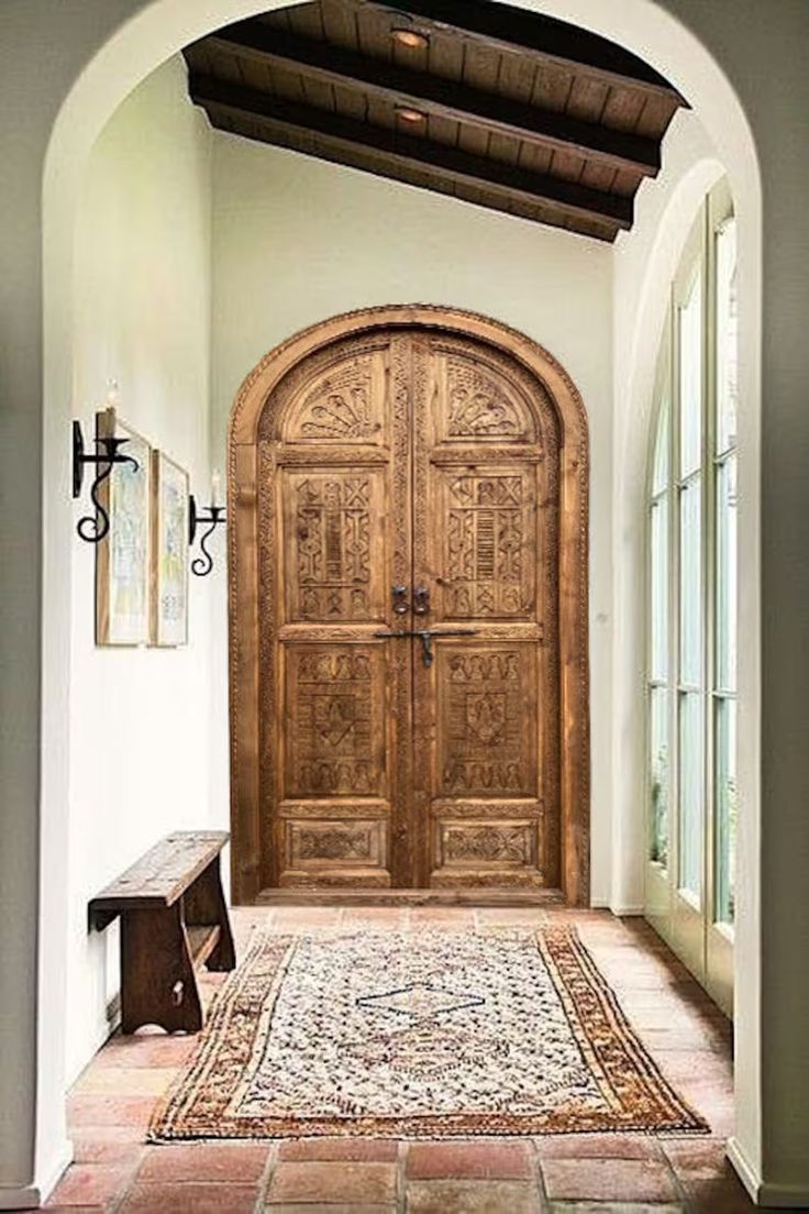 a large wooden door sitting in the middle of a hallway next to a bench and two windows