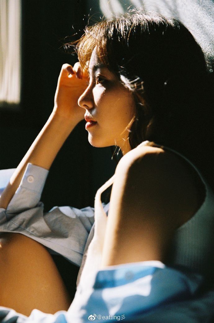 a woman sitting on top of a bed next to a window with her hand under her chin