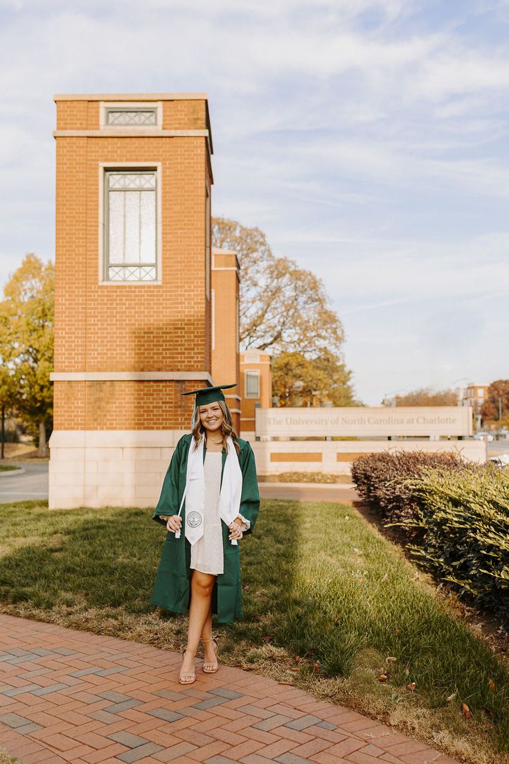 a woman standing in front of a brick building wearing a green graduation gown and cap