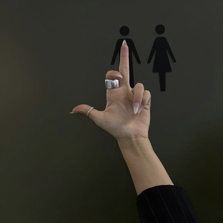 a woman's hand is pointing to the male and female silhouettes on a black wall