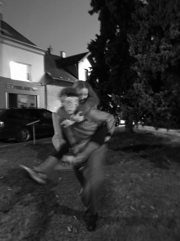 black and white photograph of two people in front of a house at night with one person holding the other