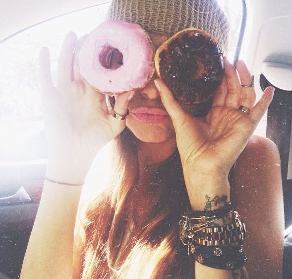 a woman holding two doughnuts up to her eyes while sitting in a car