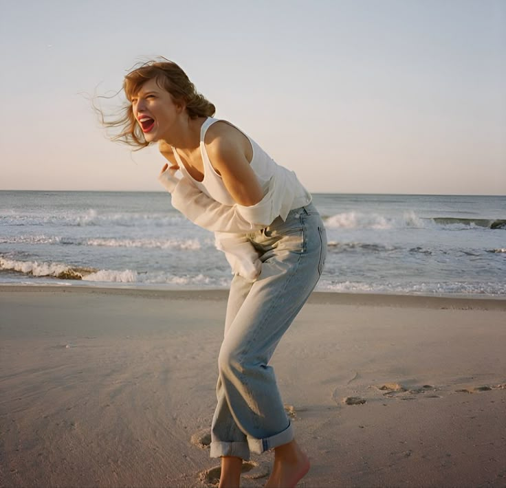 a woman standing on top of a sandy beach next to the ocean with her mouth open