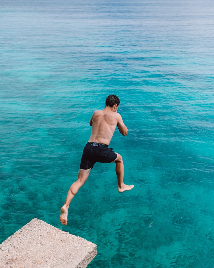 a man jumping into the water from a dock in front of some clear blue water