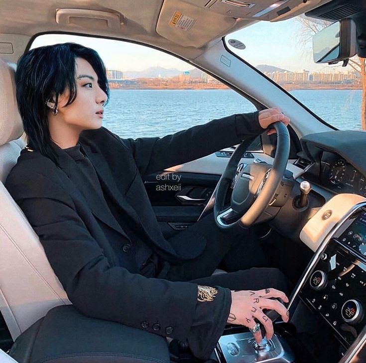 a man sitting in the driver's seat of a car with his hand on the steering wheel