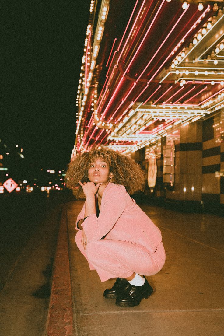 a woman kneeling on the ground in front of a building with lights all around her