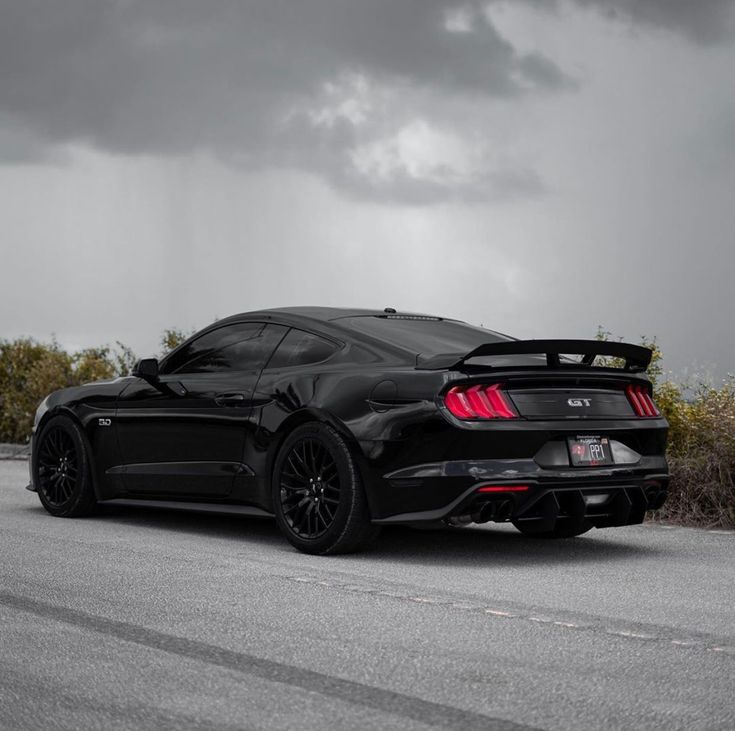 a black sports car is parked on the side of the road under a dark cloudy sky