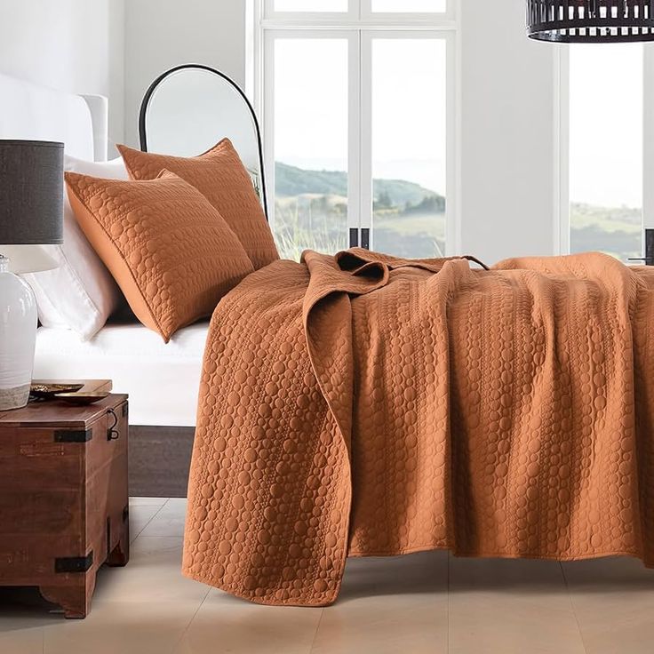 a bed covered in an orange blanket next to a window