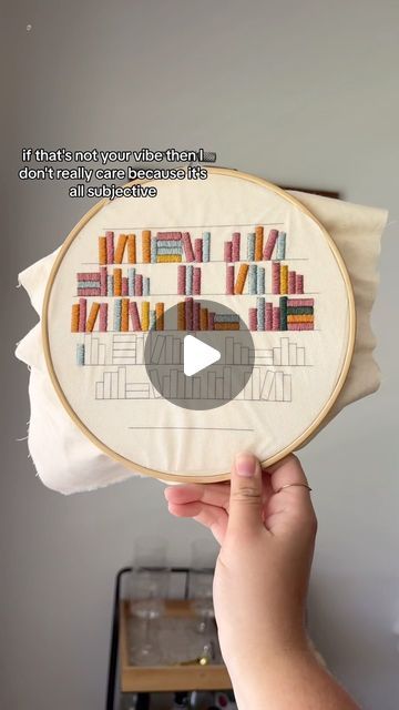 someone is holding up a cross stitch project with books on it in front of a white wall