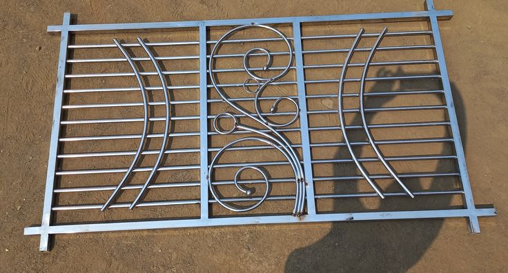 a person standing next to a metal grate on top of a dirt ground and casting a shadow