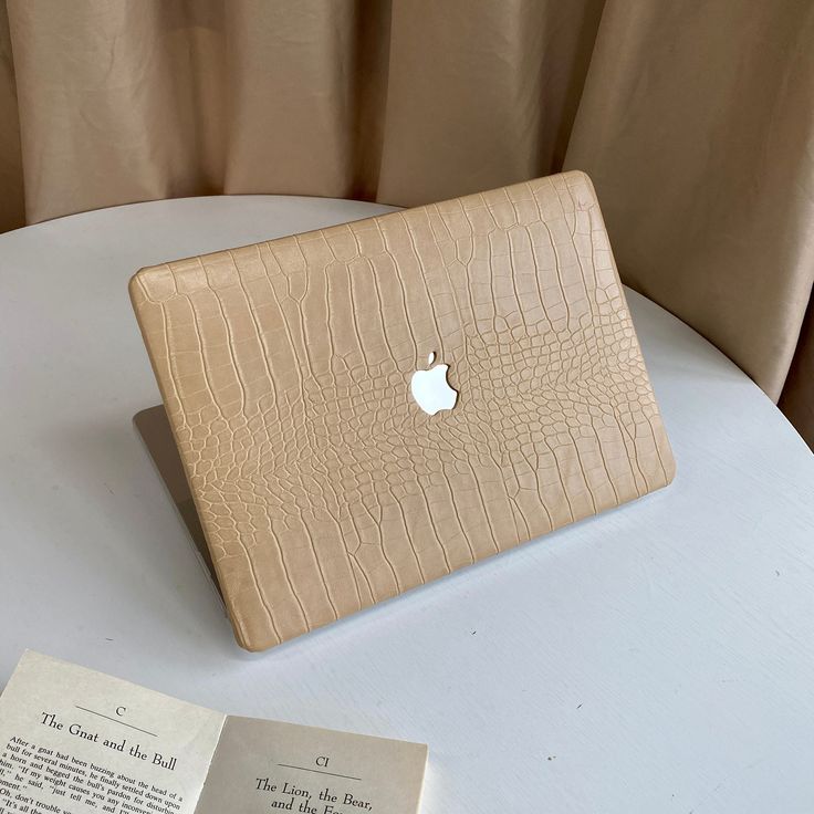 an apple laptop sitting on top of a white table next to a book and some papers