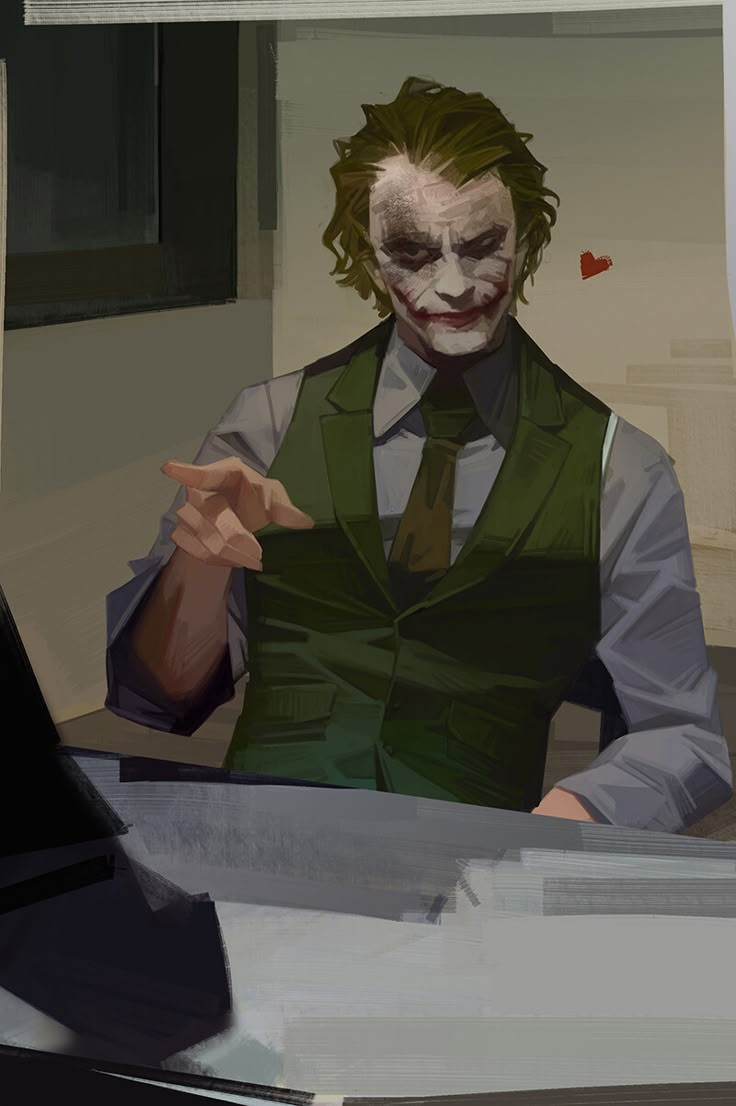 a man dressed as the joker pointing to something in his hand while sitting at a desk