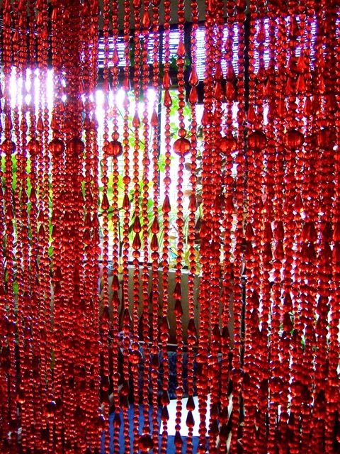 red beads hanging from the ceiling in front of a window with sunlight shining through them