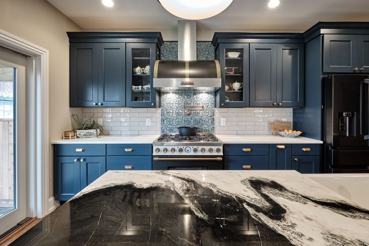 a kitchen with blue cabinets and marble counter tops, along with an island in the middle