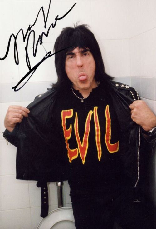 a man with long black hair is holding up a t - shirt in front of a toilet