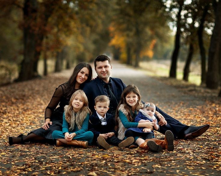 a family sitting on the ground in front of trees with leaves all around them and posing for a photo