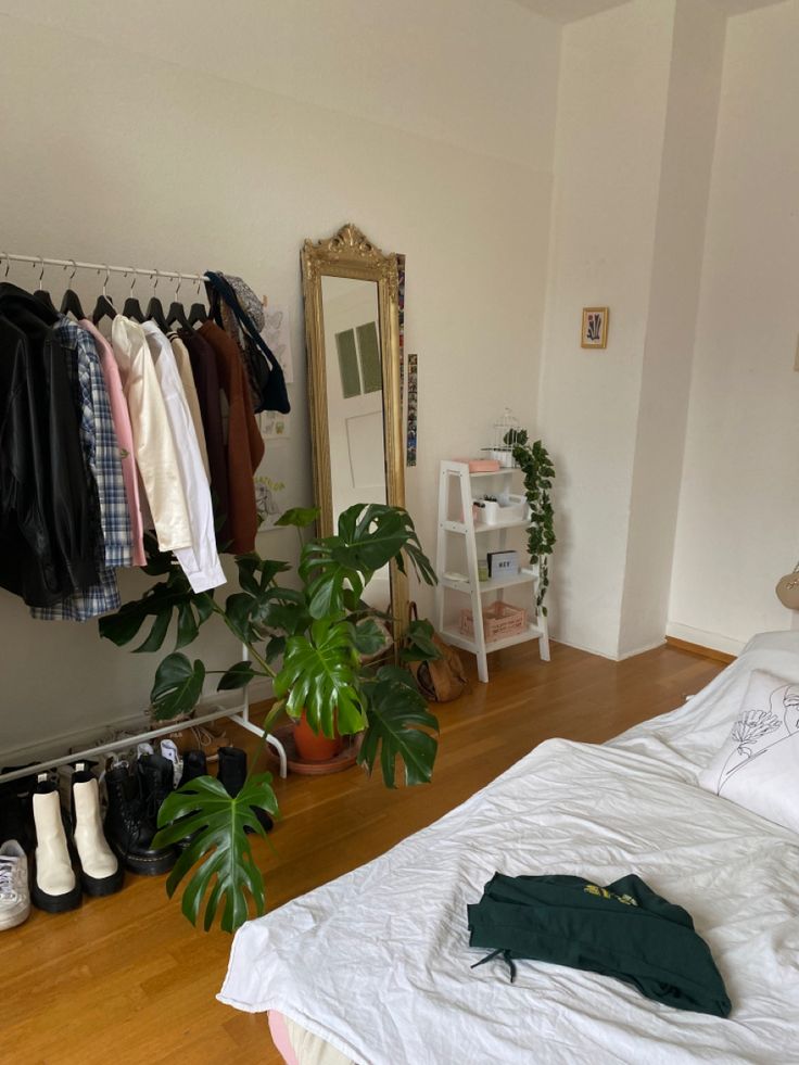 a bedroom with a bed, mirror and clothes on hangers next to a potted plant