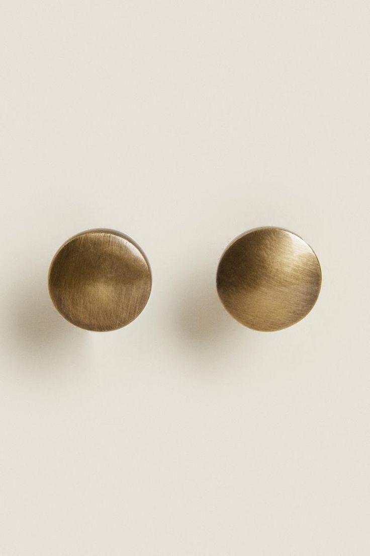 two brass - plated earrings on a white surface, one is round and the other is oval