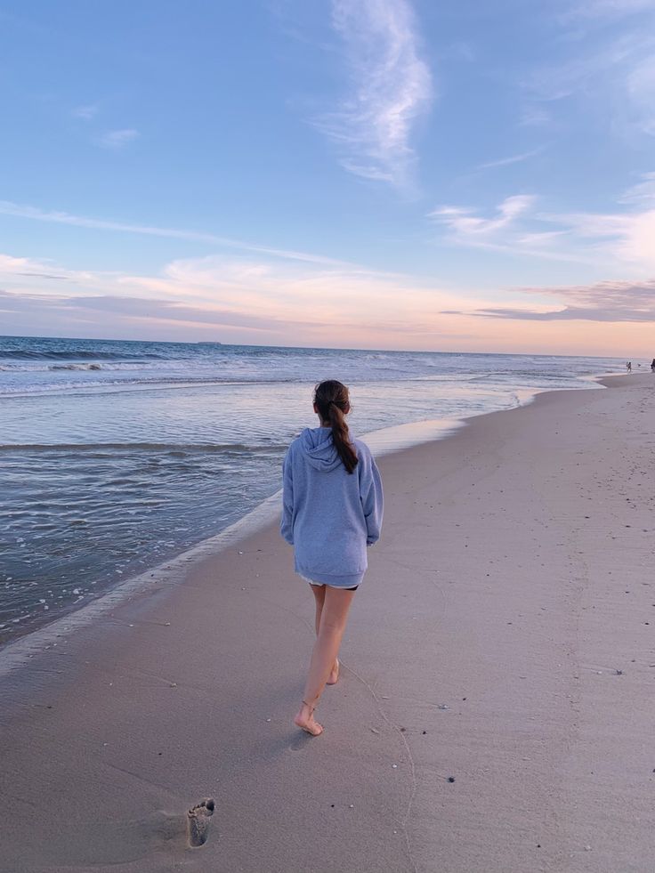 a woman walking along the beach towards the ocean