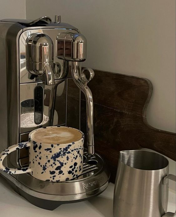 a silver coffee maker sitting on top of a counter next to a cup and saucer