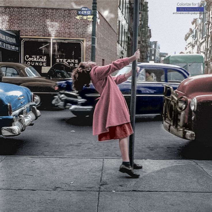 a woman leaning up against a pole on the side of a road next to parked cars