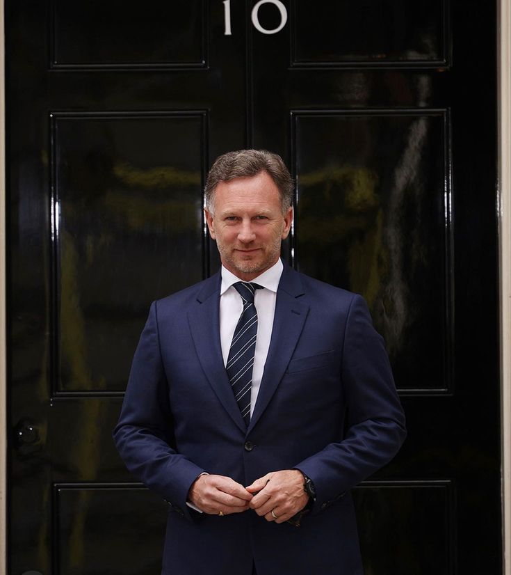 a man in a suit and tie standing by a black door with the number 10 on it