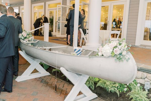 a man in a suit standing next to a boat with flowers on the side and people looking at it