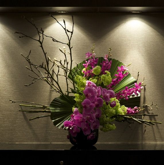 a vase filled with purple and green flowers sitting on top of a black table next to a wall