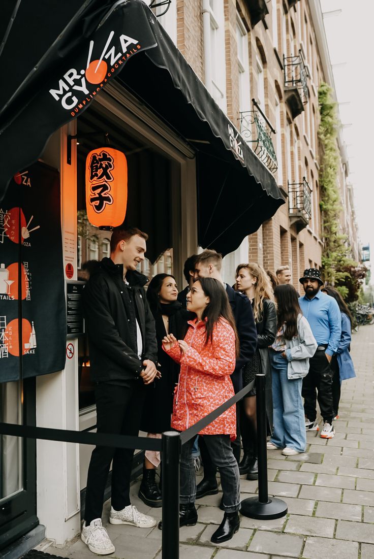 a group of people standing in front of a store on a sidewalk next to tall buildings