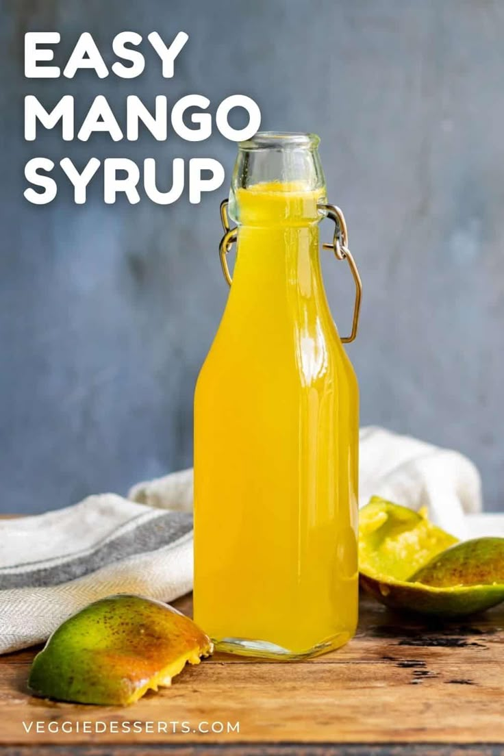 a glass bottle filled with mango syrup on top of a wooden table next to limes