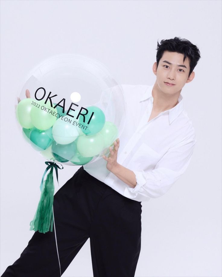 a man holding a bunch of balloons with the words okaeri on one balloon