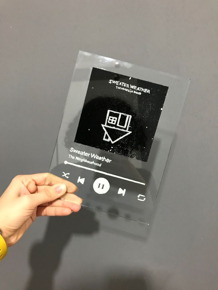 a person holding up an mp3 player in front of a gray wall with black and white stickers on it