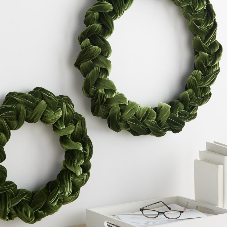 two green wreaths are hanging on the wall next to a pair of reading glasses