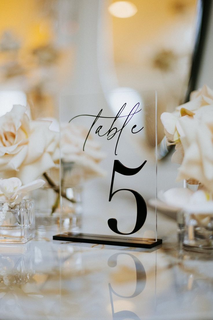 the table numbers are placed on clear acrylic plates with white flowers in vases