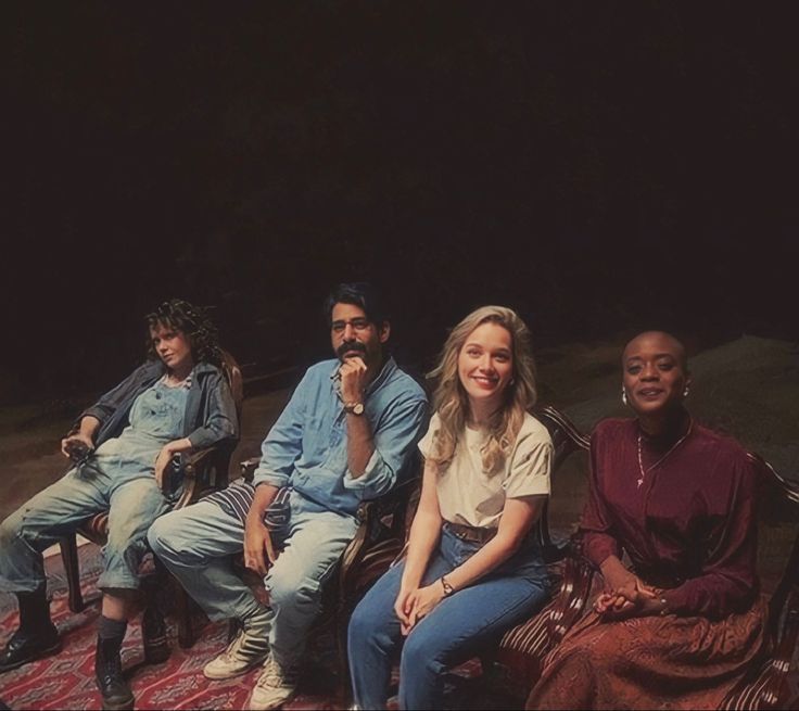 four people sitting on top of a rug in front of a dark background with one person smiling at the camera