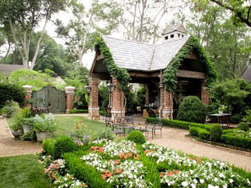 a garden with lots of flowers and greenery in front of a house that is surrounded by trees